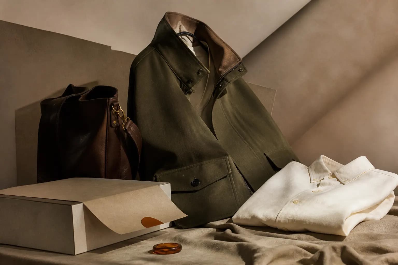 Olive jacket, cream knitwear, and leather bag in an editorial commerce display representing NOVA